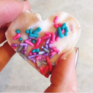 a hand holding a frozen yogurt treat shaped like a heart topped with sprinkles