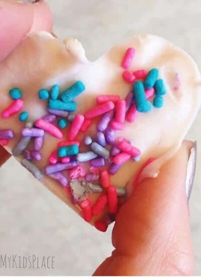 a hand holding a frozen yogurt treat shaped like a heart topped with sprinkles