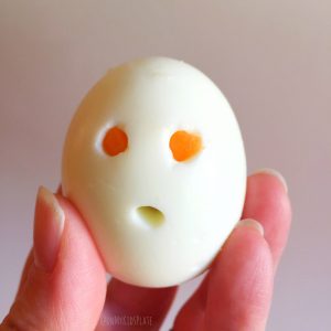 A hard boiled egg being held by a hand with holes to look like a ghost