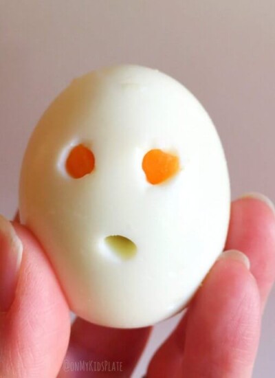 A hard boiled egg being held by a hand with holes to look like a ghost