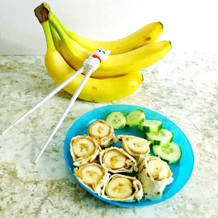 Kid's plate full of banana slices wrapped in tortilla and peanut butter with banana and kid\'s chopsticks.