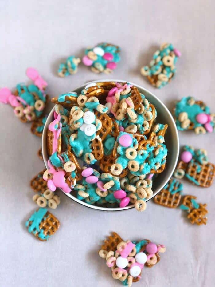 Trolls party snack mix for a birthday aprty is full of pretzels, cheerios, chocolate pieces and colorful melted turquoise and pink chocolate melts.
