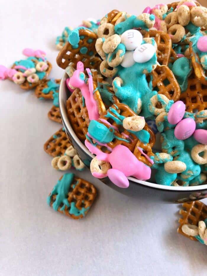 Overhead bowl of snack mix of pink and turquoise chocolate, pretzels and cereal
