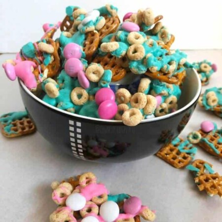 Pretzels mixed with colorful chocolate pieces, cereal pieces and melted colorful chocolate in a bowl