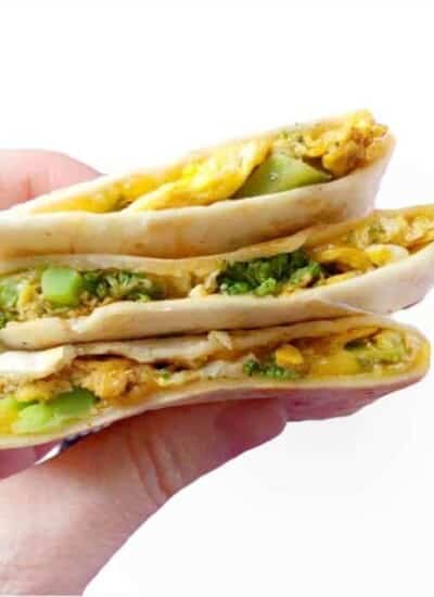 Three pieces of quesadilla stacked being held by a hand stuffed with egg, cheese and broccoli