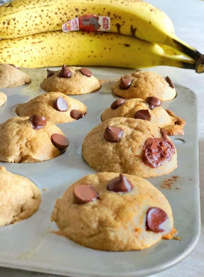 Mini muffins with chocolate chips in a pan with bananas behind