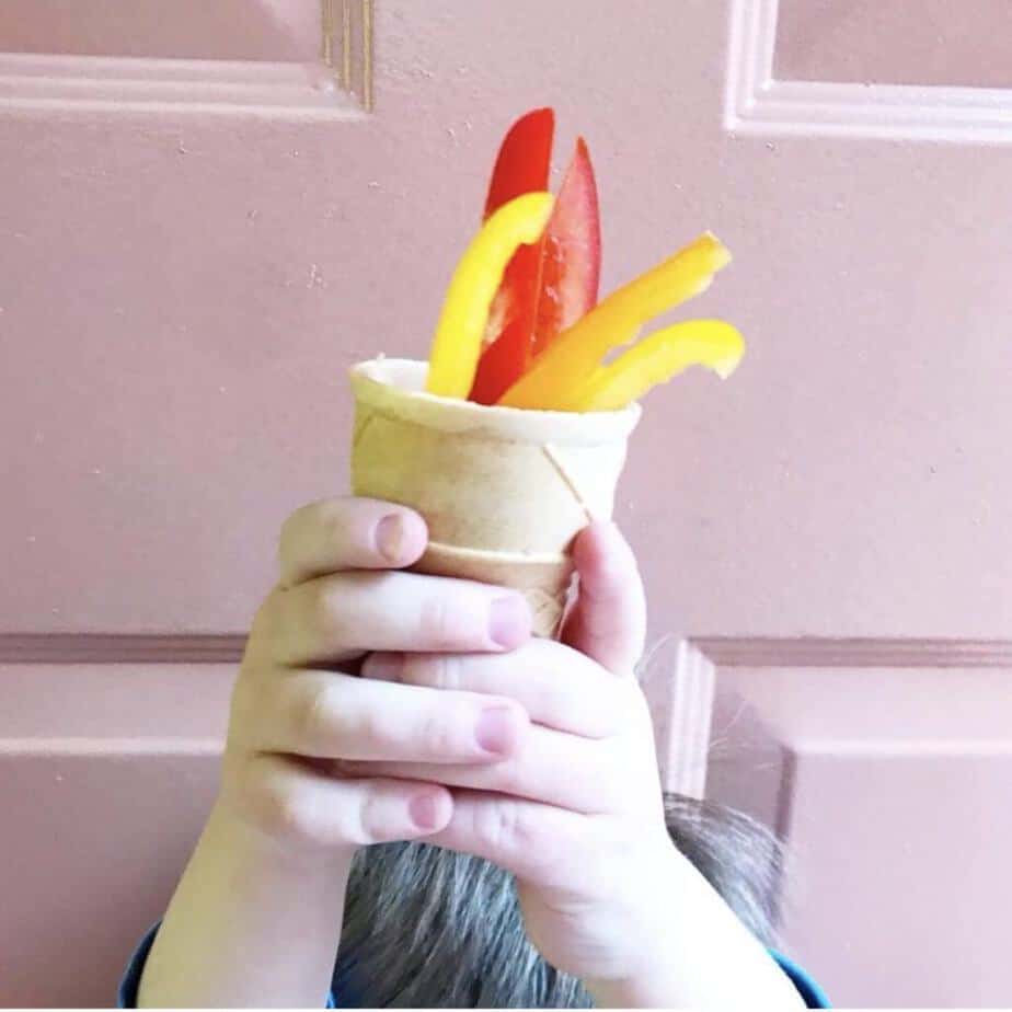 A little boy's hands holding a ice cream cone full of colorful red, orange and yellow bell peppers as if eh was holding an olympic torch.