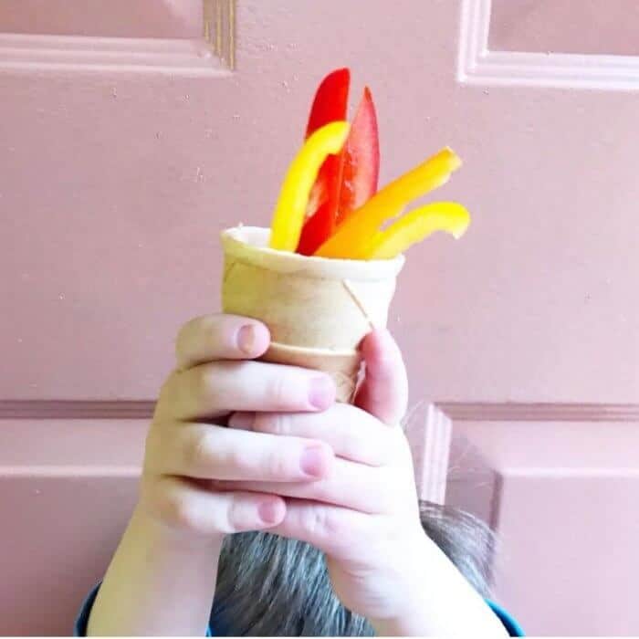 A little boy's hands holding a ice cream cone full of colorful red, orange and yellow bell peppers as if eh was holding an olympic torch.