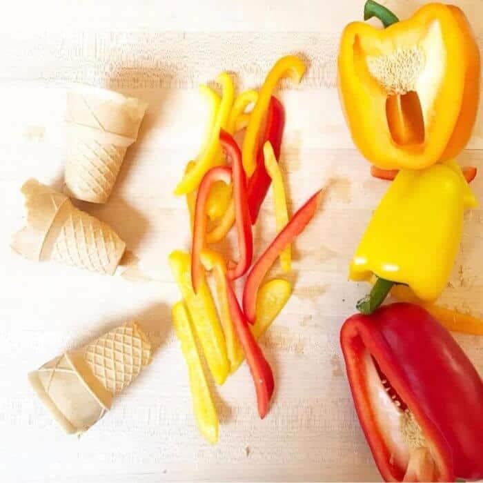 Peppers sliced into strips with ice cream cone and whole peppers on the cutting board nearby.