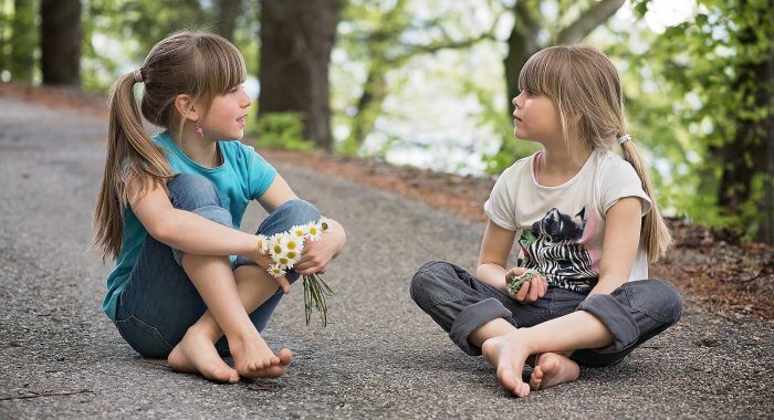 Two school age girls sitting outside, talking together.