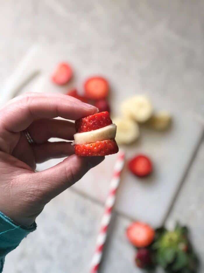 Fingers holding strawberry and banana sliced stacked.