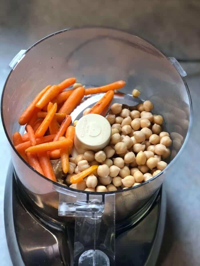 Roasted carrots and chickpeas are in a food processor from above, ready to be made into sunshine carrot veggie dip.