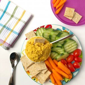 A platter of yellow dip with sliced vegetables and a child's plate with food ready to eat.