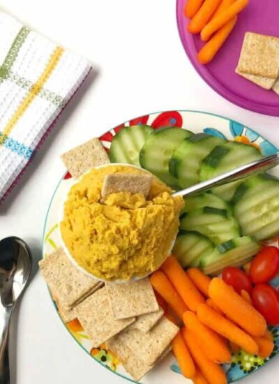 A platter of yellow dip with sliced vegetables and a child's plate with food ready to eat.