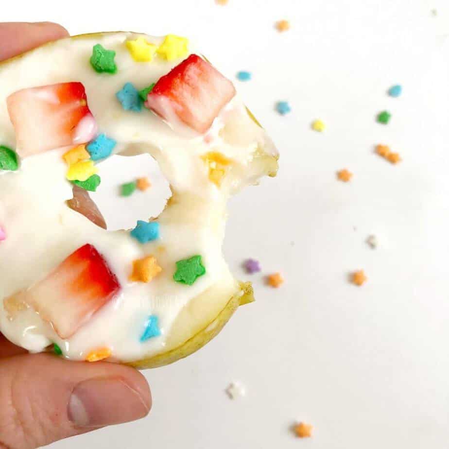 A pear covered in yogurt and decorated with sprinkles and fruit with a bite taken out of it.