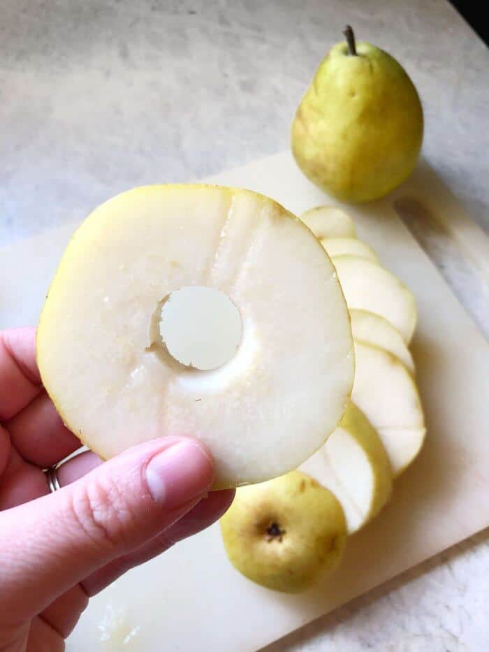 A slice of pear held up by a hand with the center core removed in a round circle