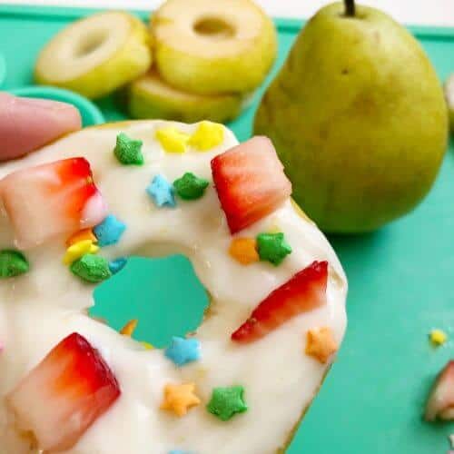 Close up of a pear slice decorated with yogurt, sprinkles and fruit pieces to look like a donut with more pear in the background