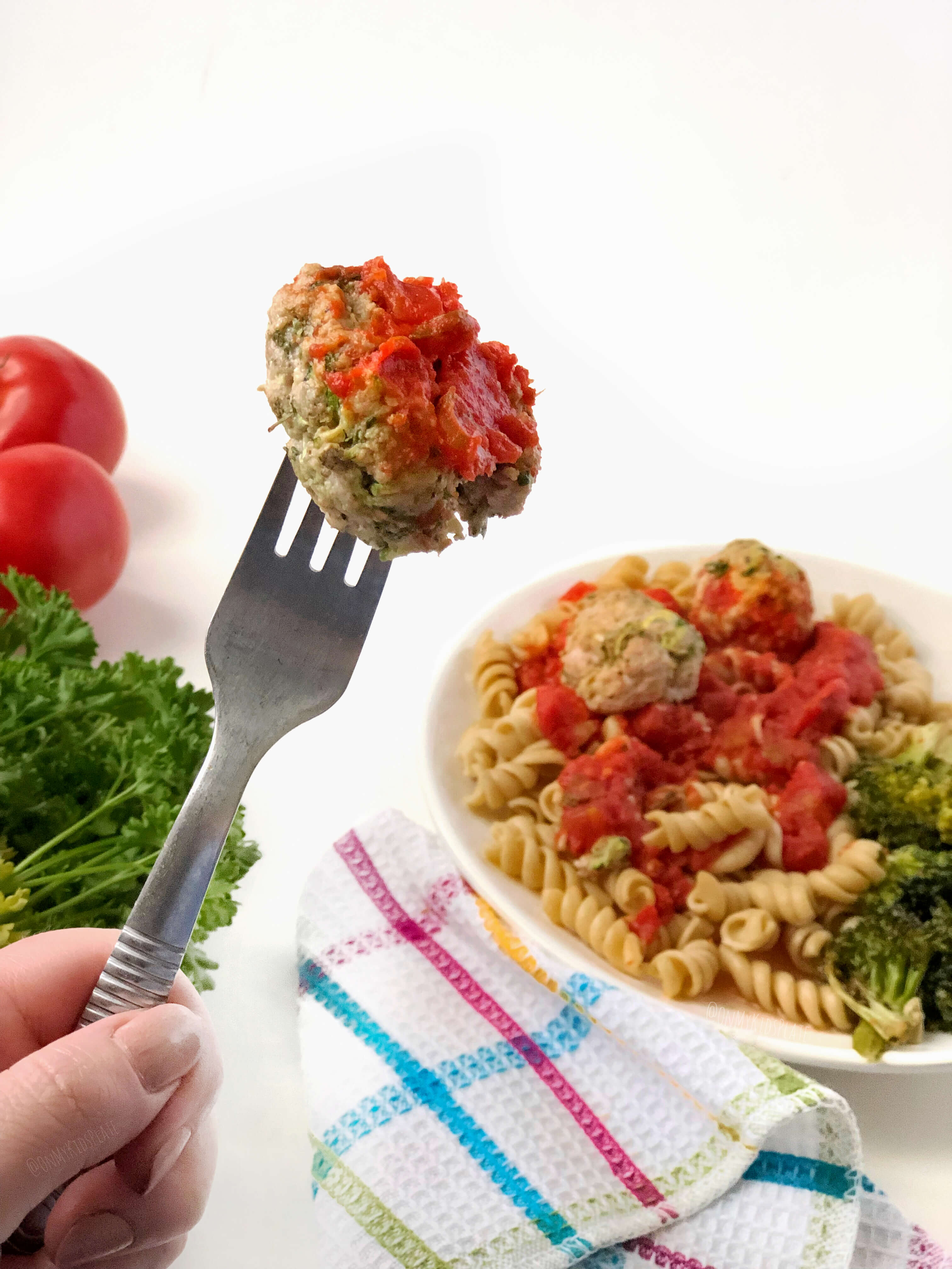 A meatball on a fork, a plate of pasta with meatballs int the background