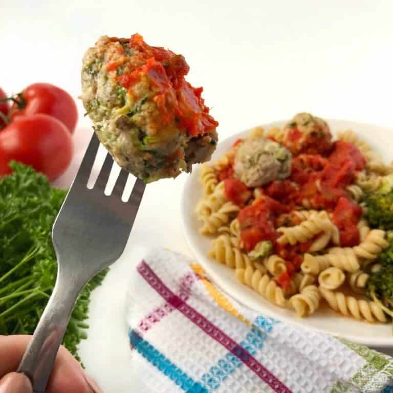 A meatball on a fork, a plate of pasta with meatballs int the background