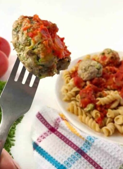 A meatball on a fork, a plate of pasta with meatballs int the background