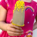 A little girl's hand holds a banana popsicle.