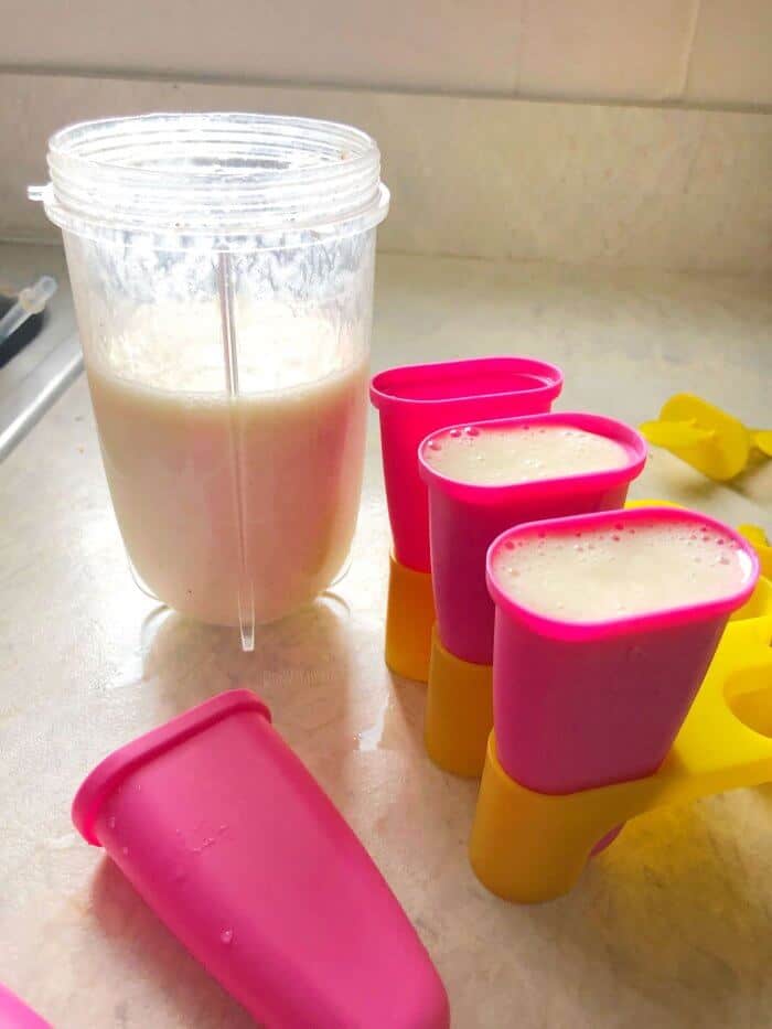 A cup full of blended popsicle mix and popsicles molds being filled