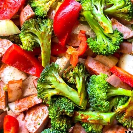 Smoked sausage mixed with roasted broccoli, peppers and onions close up on a pan.