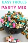 A bowl full of tasty sweet and salty sanck mix sits surrounded by colorful chocolates, Cheerios and pretzels ready for a kid's birthday party.