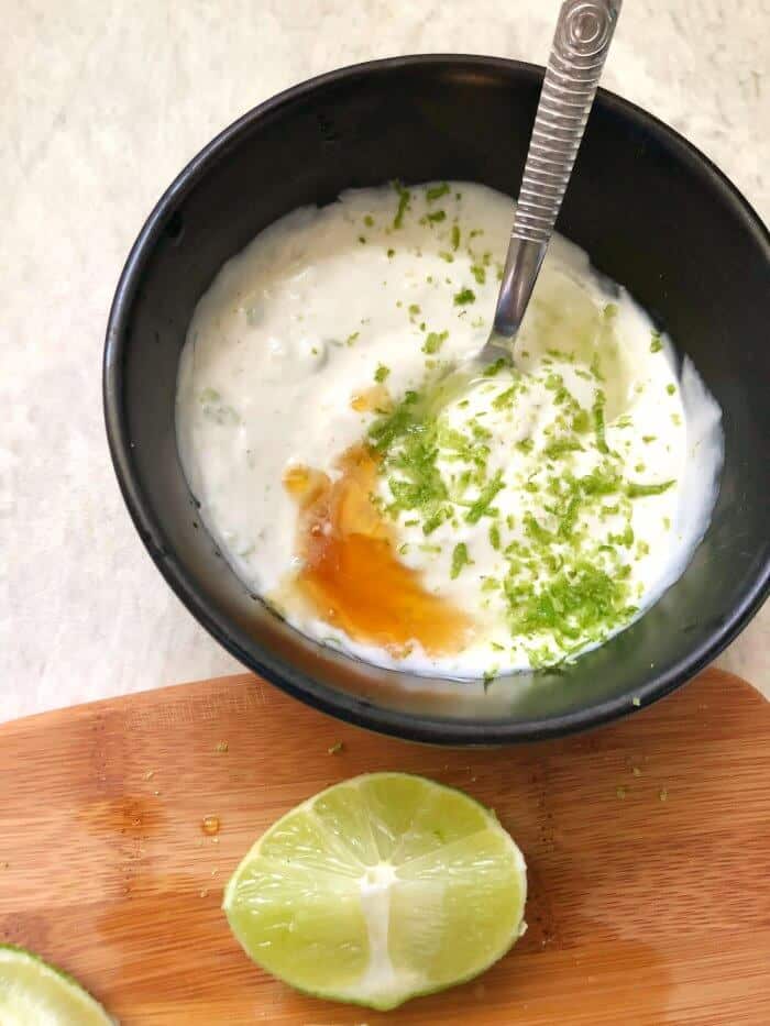 Yogurt and other ingredients being mixed in a bowl next to a slice of lime