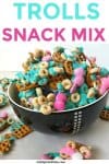 A bowl full of tasty sweet and salty sanck mix sits surrounded by colorful chocolates, Cheerios and pretzels ready for a kid's birthday party.