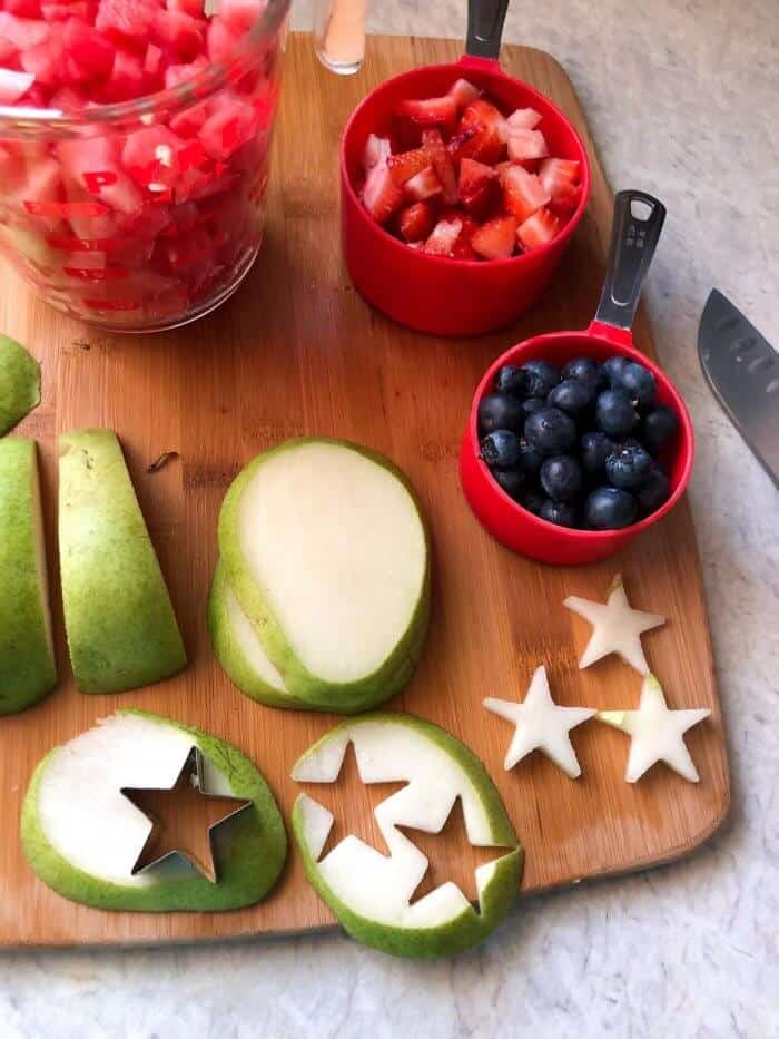 Pears, blueberries, strawberries and watermelon being sliced and prepped. Some pear is cut into small star shapes