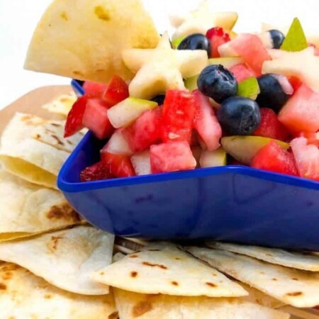Side view of fruit salsa in a star-shaped bowl with a chip dipping into it, more chips scattered around the bowl