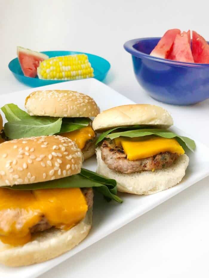 A platter of sliders with corn and watermelon in the background