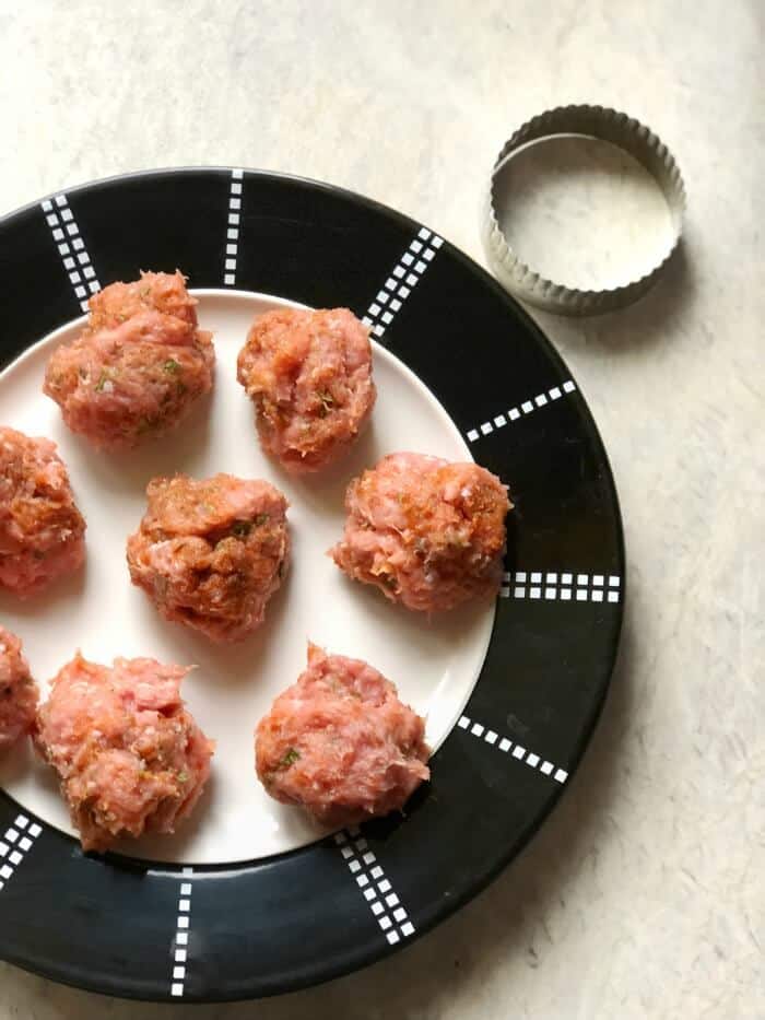 A plate of ground turkey separated in balls on a plate next to a round cookie cutter