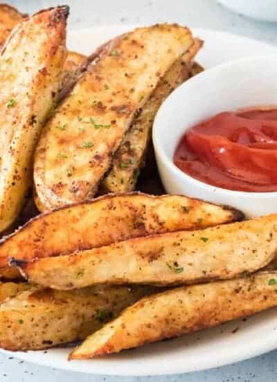Plate of seasoned potato wedges next to a small bowl of ketchup, perfect for pairing with Turkey Burger Sliders.