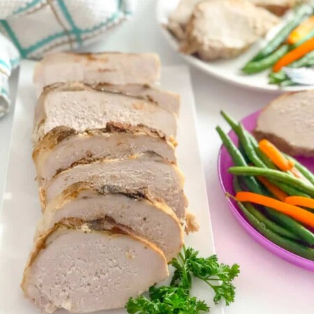 A plate of pork loin sliced on a plater next to dinner plates with vegetables