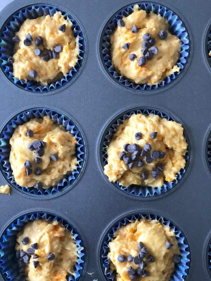 Muffin batter in a muffin tin topped with chocolate chips