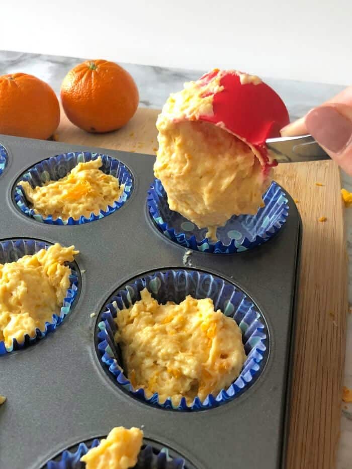 Orange muffin batter being scooped into a muffin pan.
