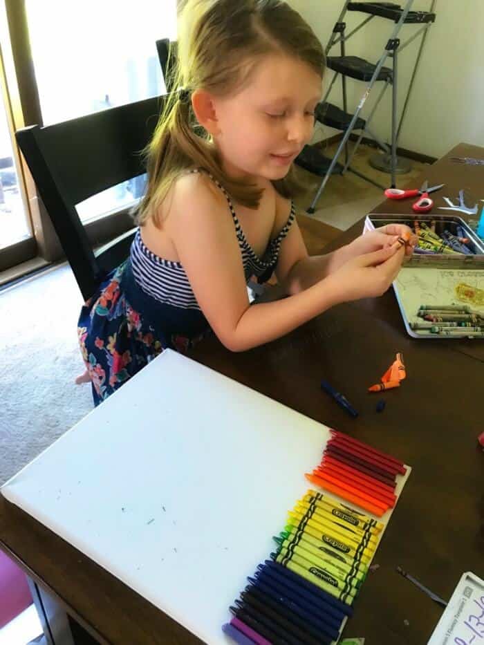 A child creating unwrapping crayons and laying them on a canvas