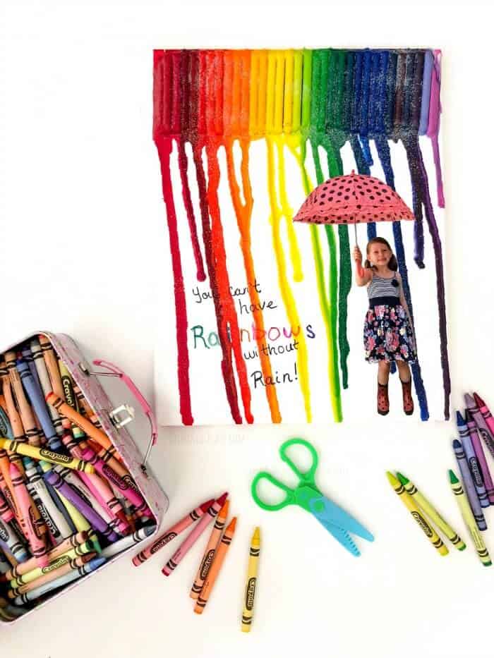 Canvas with melted crayons and a girl holding and umbrella with crayons and scissors scattered around the canvas
