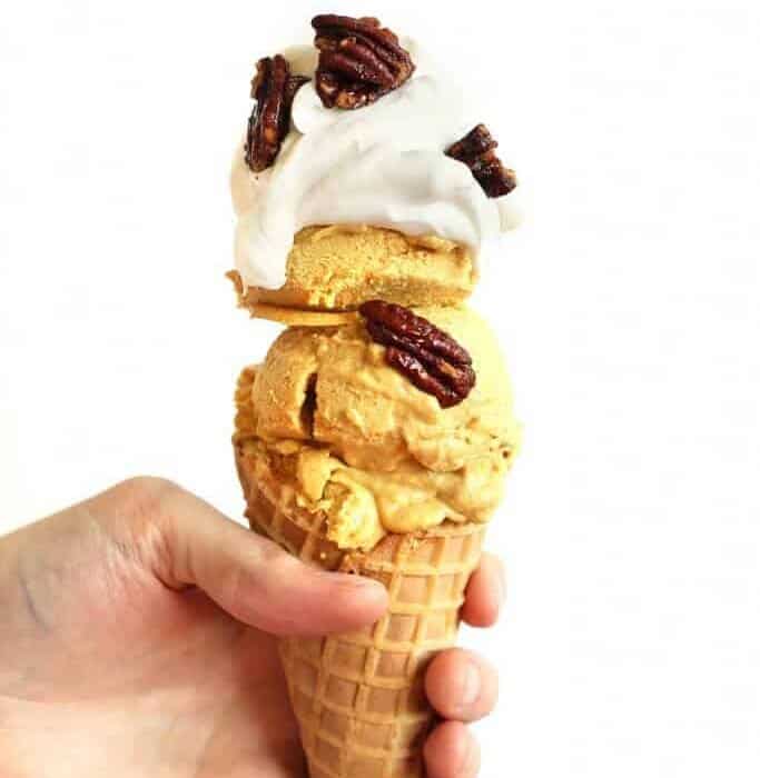 Pumpkin ice cream scooped high on a cone with a hand holding the cone.