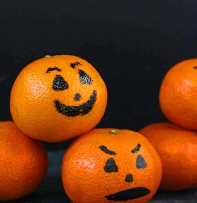 Several clementines stacked decorated to look like Jack O'Lanterns for Halloween.