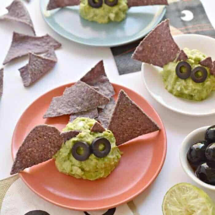 Portions of guacamole on plates decorated with olive eyes and tortilla chip wings to look like bats.