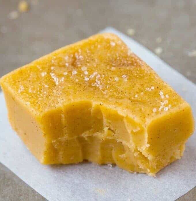 A piece of pumpkin fudge on parchment paper with a bite missing.