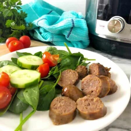 Italian sausage sliced on a plate next to a salad with an instant pot behind.