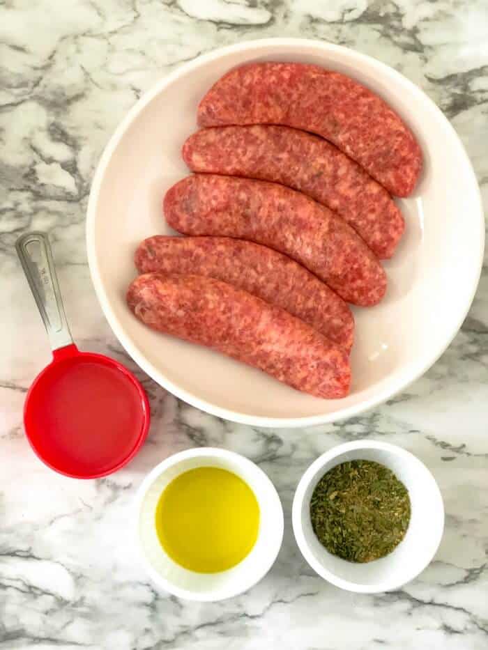 Raw sausages on a plate with oil, broth and herbs all in cups