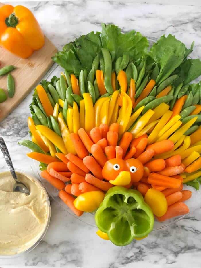 A closer view of a platter of vegetables made to look like a turkey with a container of hummus next to the platter