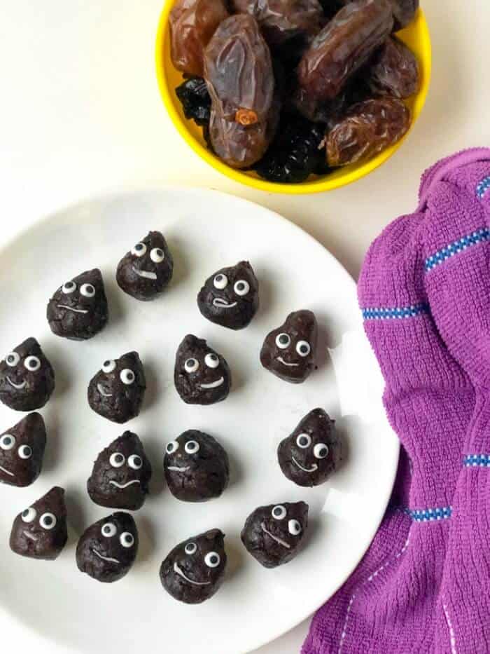 Overhead of chocolate snack bites on a plate made to look like a poo emoji with a bowl of dates next to the plate.
