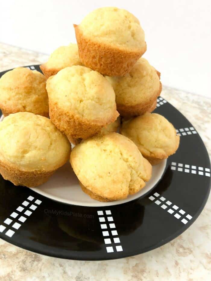 A pile of cornbread muffins sits high on a plate.