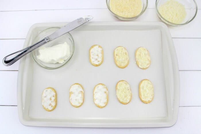 Cheese in a bowl being spread on crackers on a baking sheet